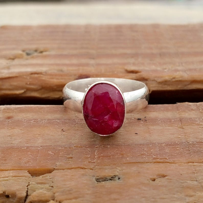 Pu&ograve; includere: Un anello d'argento con una grande gemma di rubino ovale. Il rubino &egrave; di un rosso intenso ed &egrave; incastonato in una fascia d'argento lucida. L'anello &egrave; esposto su una superficie di legno. Il design &egrave; semplice ed elegante.