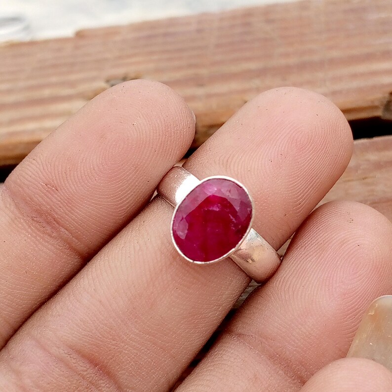 Pu&ograve; includere: Un anello d'argento con un grande rubino ovale. Il rubino &egrave; di un rosso intenso e vibrante ed &egrave; incastonato in una semplice fascia d'argento lucida. L'anello &egrave; mostrato su un dito, evidenziando le dimensioni e la brillantezza della gemma.