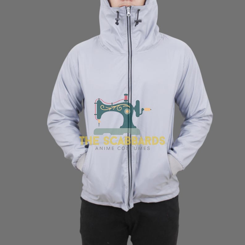 Op de afbeelding: Een lichtgrijze jas met capuchon, een ritssluiting over de hele lengte en twee voorzakken. De jas heeft een hoge kraag en een capuchon met trekkoord. De tekst "THE SCABBARDS ANIME COSTUMES" staat op de onderkant van de jas.