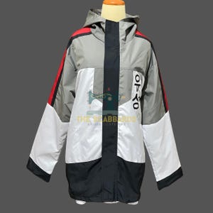 Op de afbeelding: Een hooded jack in colorblock-design in grijs, wit, zwart en rood. De jas heeft een ritssluiting aan de voorkant, een zwarte verticale streep en tekst aan de rechterkant. De mouwen hebben rode strepen. De jas wordt op een mannequin getoond.