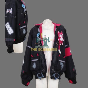 May include: A black jacket with a pink inner lining, featuring various patches including a red cat plush, flame and lightning bolt icons, and white text. The jacket has multiple pockets, silver-toned hardware, and black ribbed cuffs with red accents.