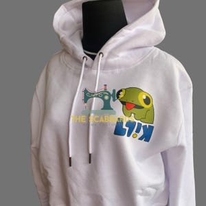 May include: White hoodie with a drawstring hood and a graphic on the front. The graphic features a green frog with a red tongue, a sewing machine, and text that reads "THE SCABBARDS" and "LY!K".