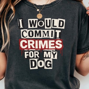 May include: Dark gray t-shirt with the text "I WOULD COMMIT CRIMES FOR MY DOG" in a bold, block letter style. The word "CRIMES" is in a red, distressed font with dripping blood effect. A casual, comfortable tee.
