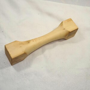 Könnte beinhalten: Ein heller Holzstift mit quadratischen Enden. Der Stift ist glatt und hat eine natürliche Holzmaserung.
