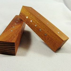 Könnte beinhalten: Zwei rechteckige Holzblöcke mit einer natürlichen Holzoptik und silbernen Punkten auf der Oberseite. Die Blöcke sind übereinander gestapelt.