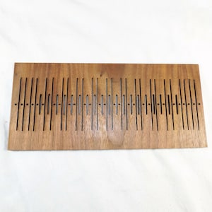 Puede incluir: Un panel de madera con un patrón repetitivo de líneas verticales cortadas en la madera. El panel es de color marrón claro.