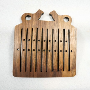 Puede incluir: Telar de madera con forma rectangular y acabado marrón. El telar tiene una serie de ranuras y agujeros verticales para tejer.