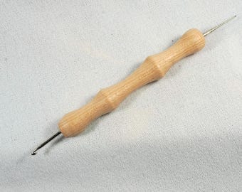 Può includere: Un uncinetto in legno con un uncino in metallo a un'estremità e un manico in legno arrotondato all'altra estremità.