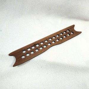 May include: A wooden, rectangular decorative piece with a series of square cutouts. The piece is a warm brown color and has a curved shape at each end. The cutouts are evenly spaced along the length of the piece.