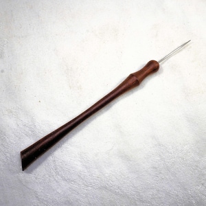 Könnte beinhalten: Ein Werkzeug aus Holz mit einem langen, schlanken Griff und einer scharfen Metallspitze. Der Griff ist dunkel rotbraun und hat eine glatte Oberfläche. Das Werkzeug liegt auf einer weißen Oberfläche.