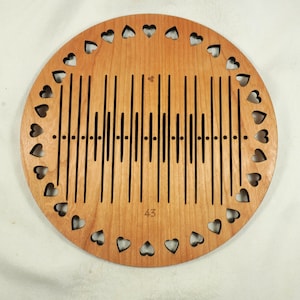 May include: A circular light brown wooden plaque featuring a laser-cut sound wave pattern across the center and a border of small heart-shaped cutouts around the perimeter. The number 43 is engraved near the bottom edge of the wooden disc.
