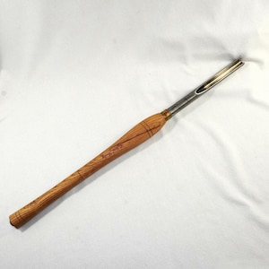 May include: A wood turning tool with a long, light brown wooden handle and a silver metal blade. The handle has a natural wood grain pattern and the text "Robert Sorby" is inscribed on the handle. The tool is designed for shaping wood.