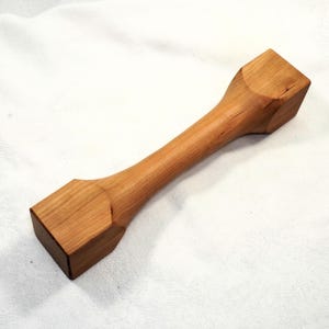 Könnte beinhalten: Ein Nudelholz aus Holz mit quadratischen Enden. Das Nudelholz ist aus hellbraunem Holz gefertigt und hat eine glatte Oberfläche.