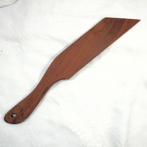 Op de afbeelding: Een houten spatel met een gebogen handvat en een breed, schuin blad. De spatel is gemaakt van roodbruin hout en heeft een gat aan het uiteinde van het handvat om op te hangen. Ontworpen voor koken en bakken.