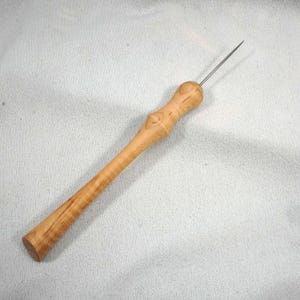 Könnte beinhalten: Eine Ahle aus Holz mit einem polierten, hellbraunen Griff und einer langen, schlanken Metallspitze. Der Griff hat eine abgerundete Oberseite und ein sich verjüngendes Design. Die Ahle wird wahrscheinlich zum Durchstechen oder Markieren von Materialien verwendet.