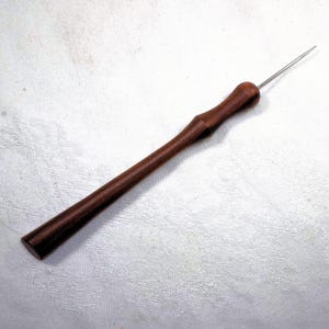 Könnte beinhalten: Ein Holzwerkzeug mit einem langen, schlanken Griff und einer scharfen, spitzen Metallspitze. Der Griff ist dunkelbraun und hat eine glatte, polierte Oberfläche.