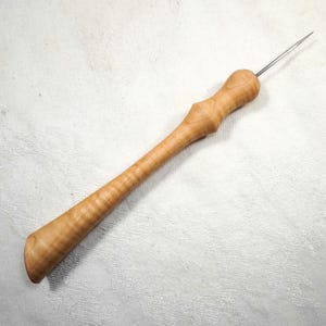 Könnte beinhalten: Ein Holzwerkzeug mit einem langen, schlanken Griff und einer scharfen Metallspitze. Der Griff ist aus hellem Holz mit natürlicher Maserung. Das Werkzeug wird für Handwerk und Hobbys verwendet.