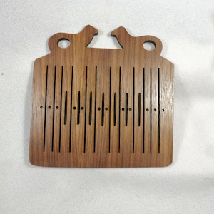 May include: Wooden tea bag holder with a light brown finish. The holder features vertical slots and two decorative animal silhouettes at the top, with two circular holes. The design is simple and elegant.