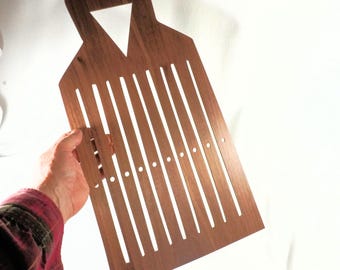 May include: A wooden weaving tool with a handle and a triangular cutout. The tool has vertical slots and small circular holes. The wood is a warm brown colour.