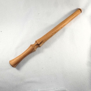 May include: A handcrafted wooden wand with a light brown finish. The wand features a detailed handle with a carved design and a smooth, tapered shaft. The tip of the wand has a black ring. The wand is approximately 14 inches long.