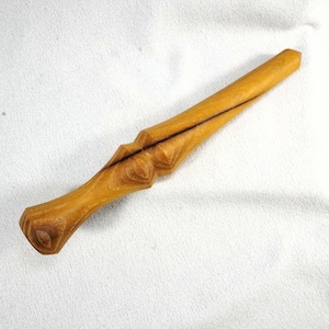 May include: A handcrafted wooden wand with a light brown finish. The wand features a detailed handle and a dark line running down the center. The wand is approximately 12 inches long.