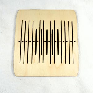 May include: A wooden loom with a black and white design. The loom has a series of vertical lines and a few horizontal lines.