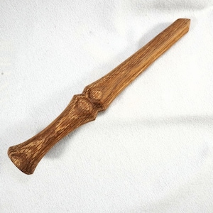 May include: A handcrafted wooden wand with a textured, brown finish. The wand features a flared handle, a decorative midsection, and a tapered tip. The wood grain is visible throughout the wand's length, adding to its natural aesthetic.