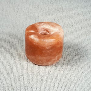 May include: A cylindrical orange salt stone bead with a smooth, polished surface and a central circular hole. The stone features natural variations in color, ranging from light peach to deep burnt orange, with a translucent, crystalline texture.