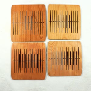 May include: Four square wooden coasters with a light brown finish. Each coaster features a unique design of vertical black lines and dots, creating a sound wave pattern. The coasters are arranged in a square formation.