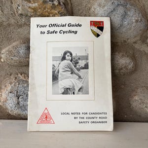 Könnte beinhalten: Vintage-Buch mit dem Titel "Your Official Guide to Safe Cycling". Das Cover zeigt ein Schwarz-Weiß-Foto einer Person auf einem Fahrrad. Zusätzlicher Text enthält "Local Notes for Candidates" und ein Radfahr-Logo.