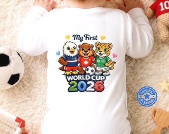 May include: A white long-sleeve baby bodysuit featuring a graphic of an eagle, a beaver, and a leopard wearing football kits. The text reads My First WORLD CUP 2026. The design includes small hearts and a football, printed on the back of the garment.