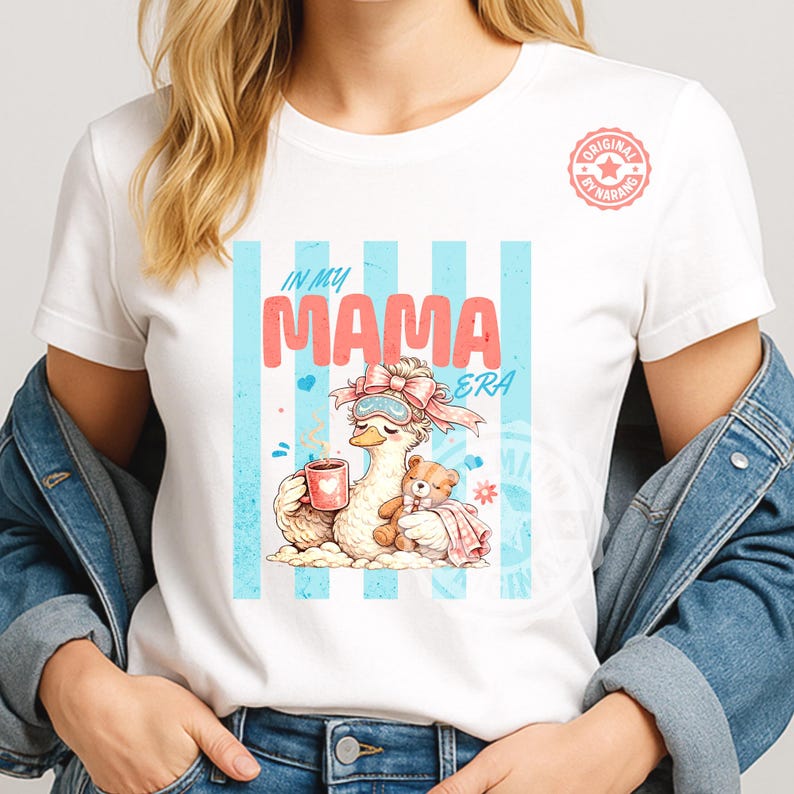 May include: White t-shirt with a graphic of a cartoon goose wearing a sleep mask and holding a mug, with a teddy bear. The text "IN MY MAMA ERA" is above the goose, with blue stripes in the background.