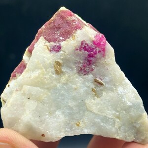 Op de afbeelding: Een ruwe, ongeslepen edelsteen met een matrix van witte kwarts en levendige roze toermalijnkristallen. De toermalijn is geconcentreerd in vlekken en aders door de steen, wat een opvallend contrast creëert. Kleine, goudbruine minerale insluitsels zijn ook zichtbaar.