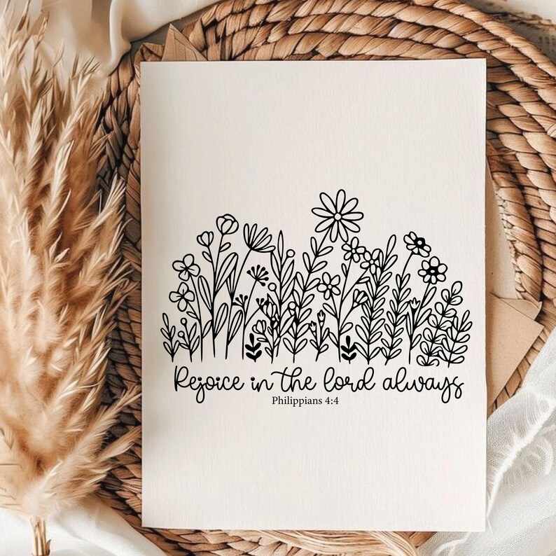 May include: A cream-colored card features a black floral illustration at the top and the text "Rejoice in the Lord always" with "Philippians 4:4" below. The card is set against a woven background with dried plants.