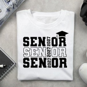 May include: White t-shirt with the word "SENIOR" stacked three times in bold black letters. The year "2027" is printed vertically on the right side of the word "SENIOR". A black graduation cap is above the last "OR".