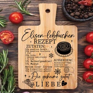 May include: A wooden cutting board with a handle, featuring a recipe for Elisen Lebkuchen. The recipe is written in German with ingredients listed. The board has a decorative design with a cake illustration and the word "LIEBE".