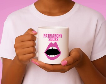 Może przedstawiać: Biały ceramiczny kubek z różowym napisem "PATRIARCHY SUCKS" nad różową grafiką otwartych ust. Kubek trzymany jest przez osobę w białej koszulce na różowym tle.