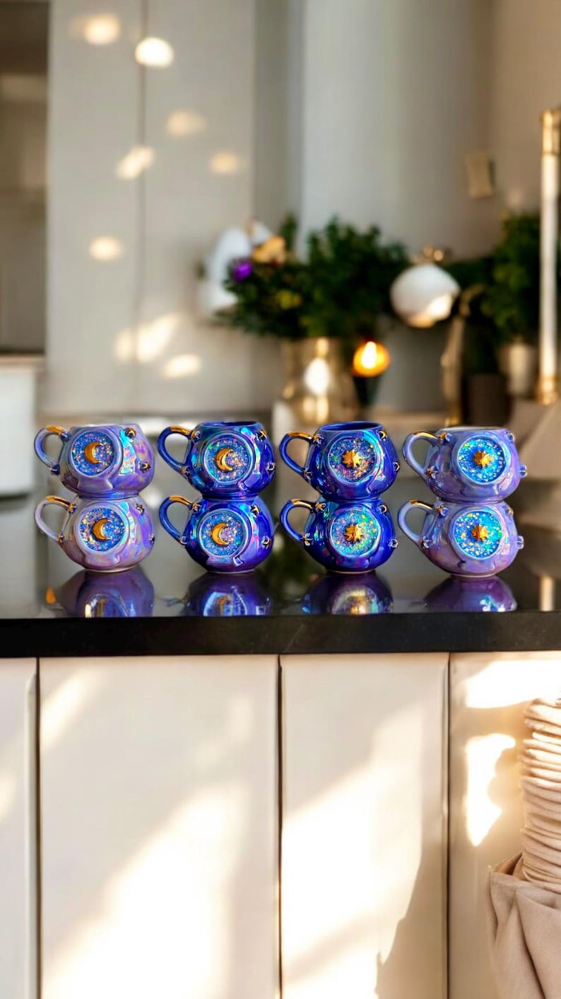 May include: A collection of eight iridescent ceramic mugs with celestial designs. Each mug features a blue and purple color scheme, gold handles, and a sun, moon, and star motif. The mugs are stacked in pairs on a dark countertop.