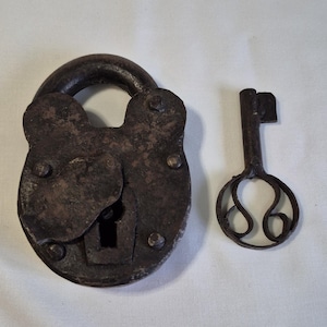 May include: An antique, weathered padlock and key set. The padlock is a dark, rusty brown with a rounded shape and visible rivets. The key has an ornate, openwork design. The items are set against a white background.