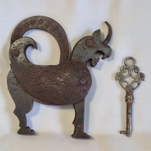 May include: An antique, ornate metal lock in the shape of a mythical creature, with a matching key. The lock has a detailed design with a curved top and a keyhole. The key is also metal, with an intricate, openwork design.