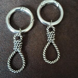 May include: Two silver-toned metal keychains, each featuring a circular spring-gate ring attached to a dangling charm shaped like a twisted rope noose. The metal has a polished finish, and the rope texture is detailed with visible twisted strands.