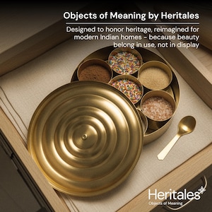 May include: A gold-colored spice box with a lid, containing various spices and a small spoon. The box is open, revealing compartments filled with brown, pink, and colorful ingredients. The text "Objects of Meaning by Heritales" is visible.