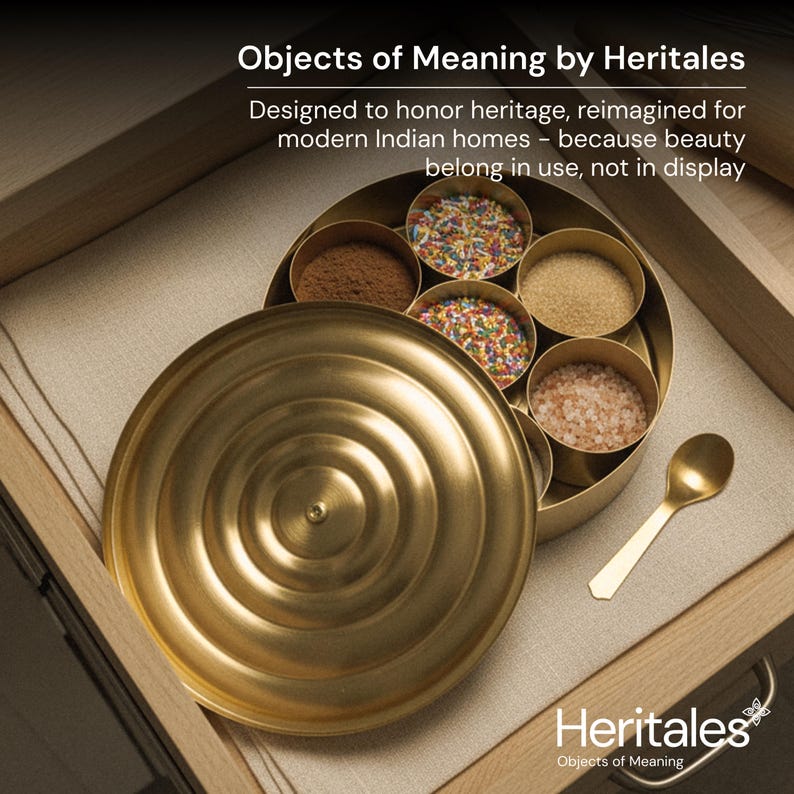 May include: A gold-colored spice box with a lid, containing various spices and a small spoon. The box is open, revealing compartments filled with brown, pink, and colorful ingredients. The text "Objects of Meaning by Heritales" is visible.