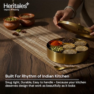 May include: A gold-colored spice container with a lid, filled with various spices. The container sits on a woven mat, with small terracotta bowls and spices in the background. Text on the image reads: "Built For Rhythm of Indian Kitchen."