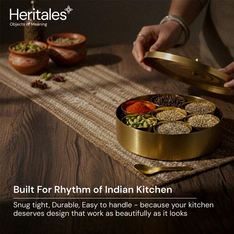 May include: A gold-colored spice container with a lid, filled with various spices. The container sits on a woven mat, with small terracotta bowls and spices in the background. Text on the image reads: "Built For Rhythm of Indian Kitchen."