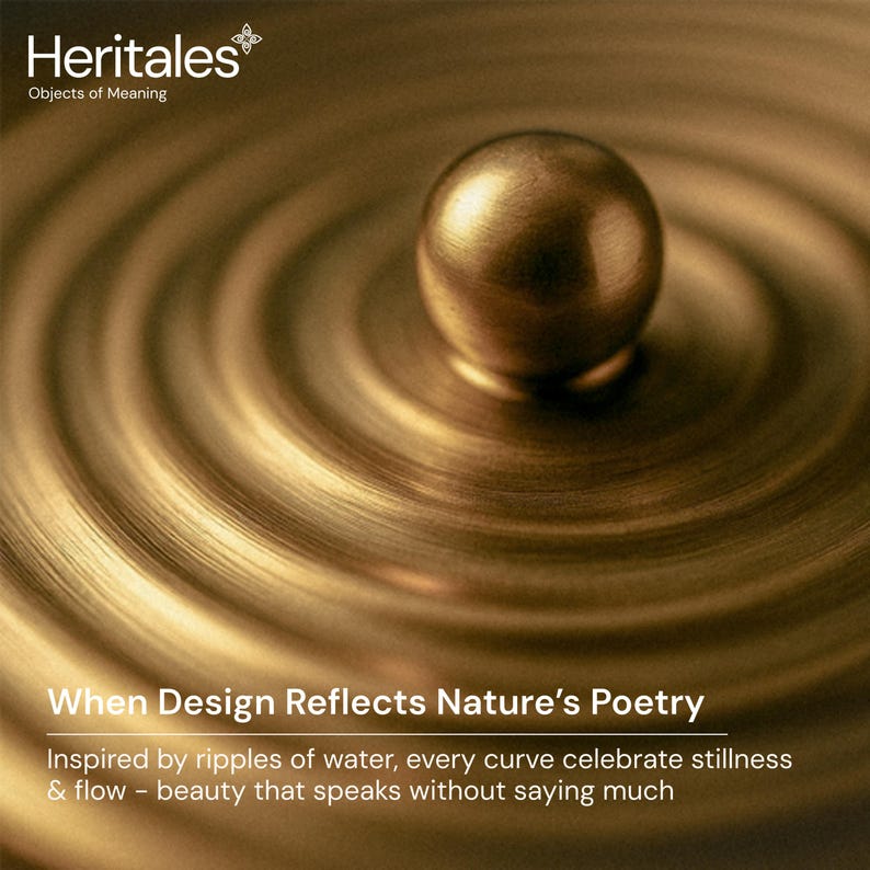 May include: A close-up of a brass-colored object with a spherical top and a circular base. The base has concentric circular ridges, creating a ripple effect. The text "Heritales Objects of Meaning" is at the top, and "When Design Reflects Nature's Poetry" is at the bottom.