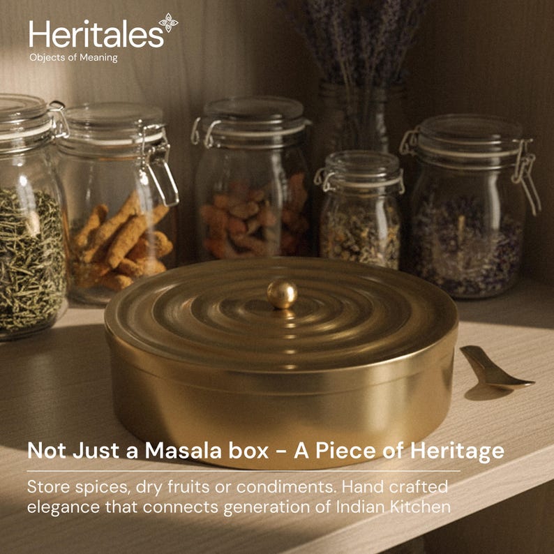 May include: A gold-colored masala box with a round lid and a small knob, surrounded by glass jars filled with spices. The text "Heritales Objects of Meaning" is at the top. The text "Not Just a Masala box - A Piece of Heritage" is at the bottom.