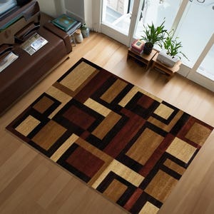 Peut inclure: Un tapis rectangulaire avec un motif géométrique dans les tons de marron, beige et noir. Le tapis présente une série de formes rectangulaires et carrées disposées dans un design abstrait. Le tapis est posé sur un parquet.