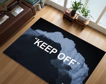 May include: A rectangular black rug with the words "KEEP OFF" in white. The rug features a cloud-like design in shades of gray and white. The rug also has text that reads "IKEA c/o Virgil Abloh Flooring Almhult, Sweden c.2019".