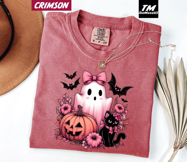 Pode incluir: Camiseta carmesim com um gr&aacute;fico tem&aacute;tico de Halloween. O design inclui um fantasma com um la&ccedil;o rosa, uma ab&oacute;bora esculpida, um gato preto e morcegos. A camisa tem gola redonda e uma etiqueta Comfort Colors.